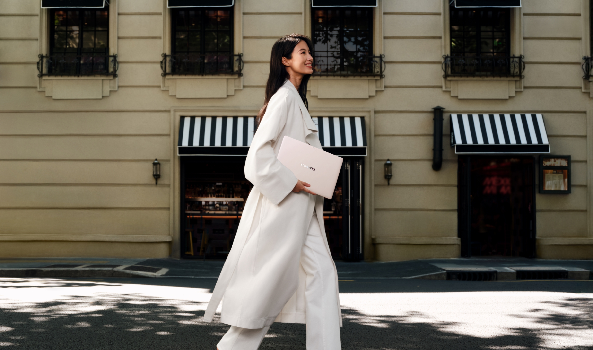 一名女性手持 HUAWEI MateBook Pro 在街上漫步，展示了轻薄