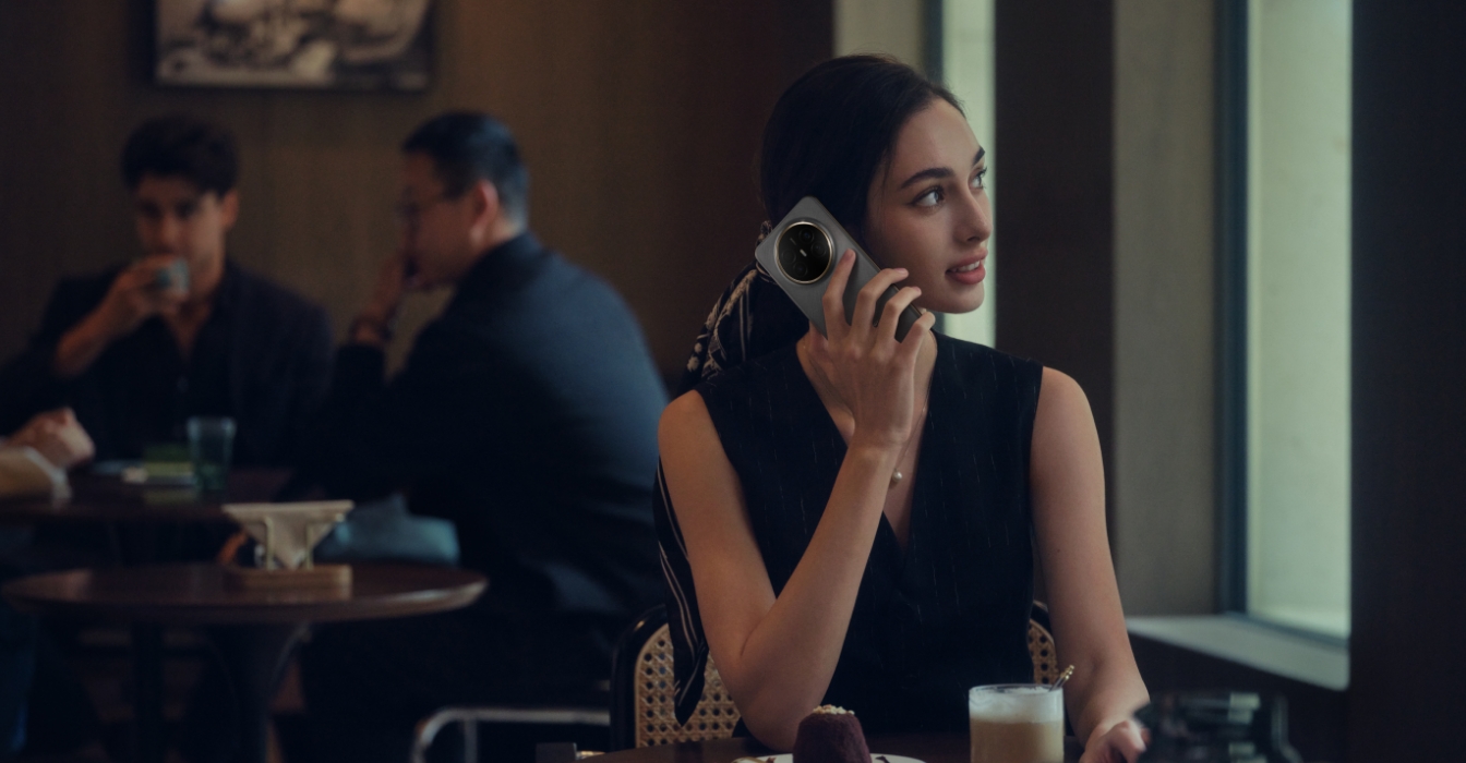 一名女性在嘈杂的场合拿着 HUAWEI Mate 70 Air 正在接听电话