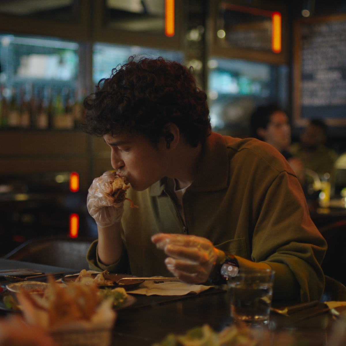 一个佩戴 HUAWEI WATCH 5 的男人正在吃披萨，双手不方便触碰手机屏幕，通过手指操控来切换手机视频